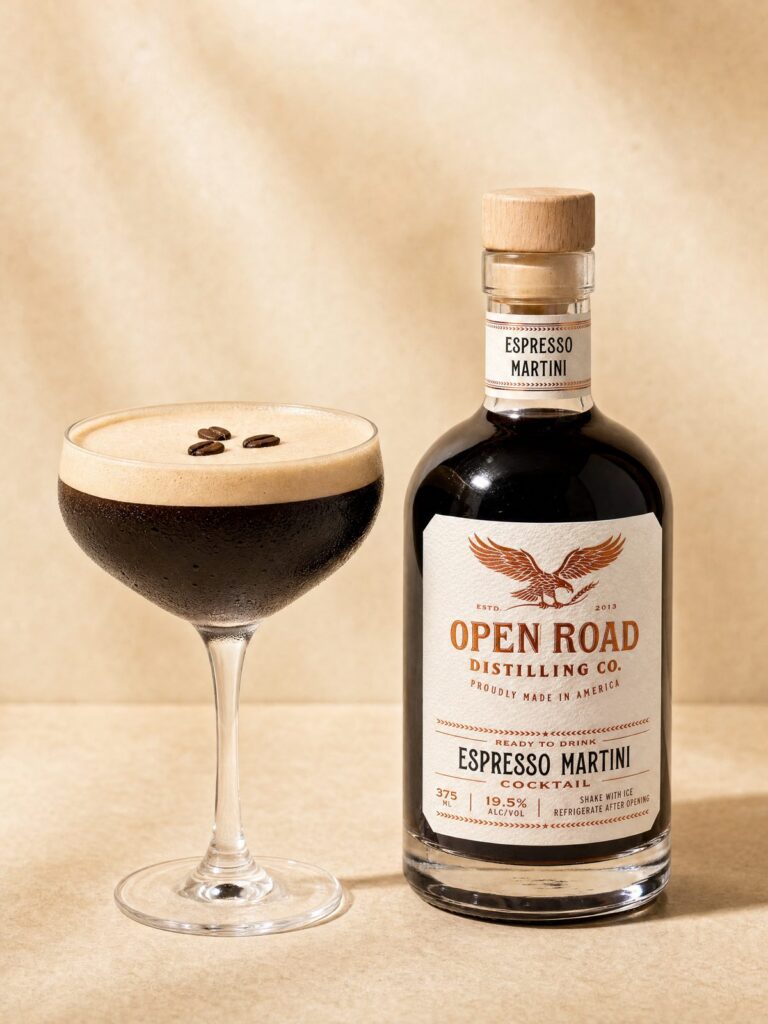 Open Road Distilling Co. ready-to-drink espresso martini poured into a foamy coupe with three espresso beans beside the 375 ml bottle